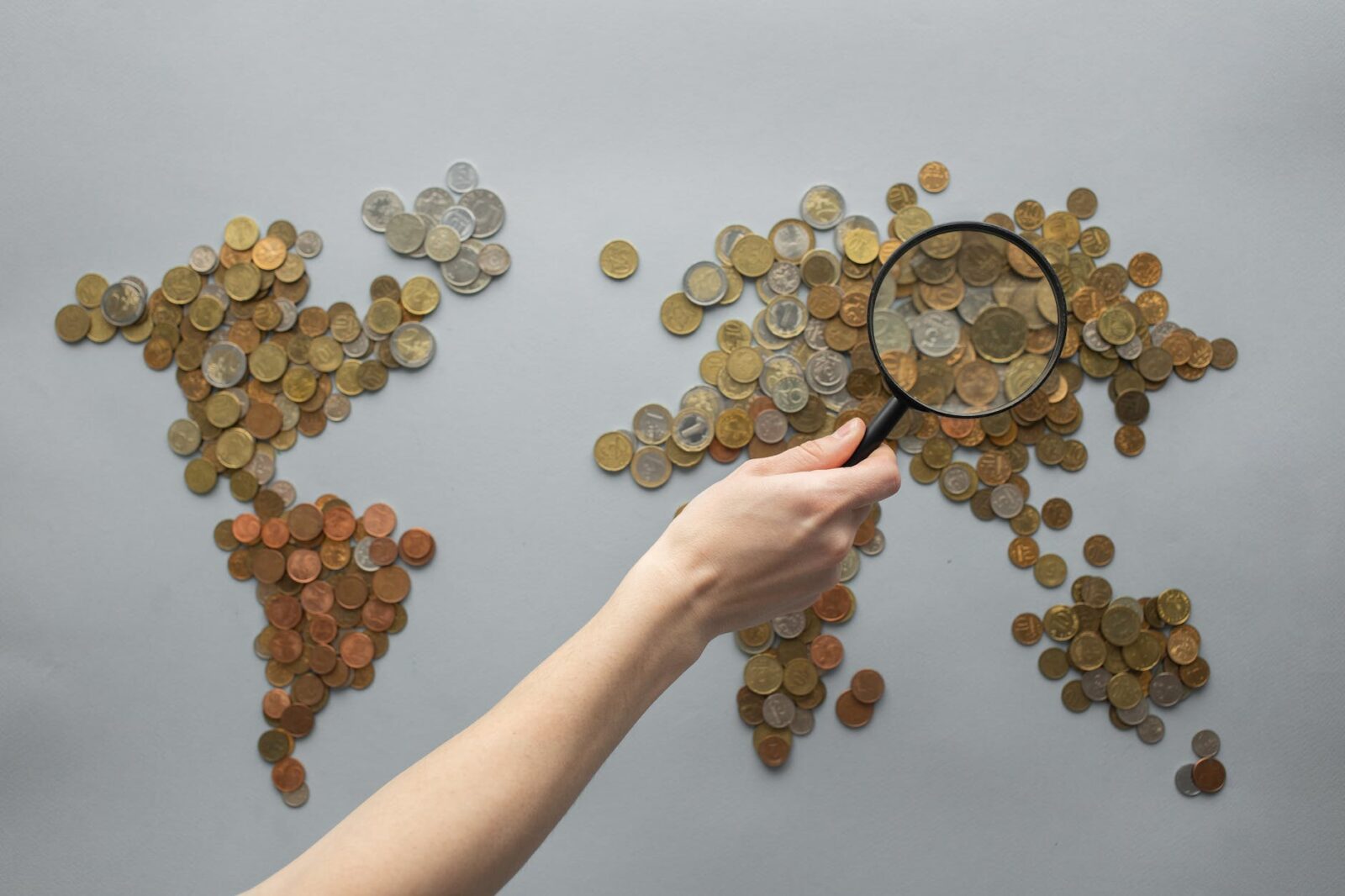 anonymous person magnifying view of coins shaped in world map